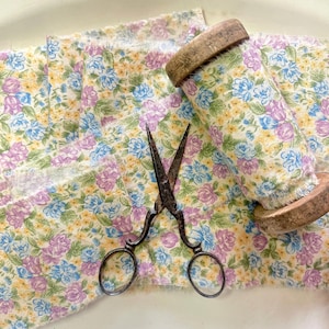 May include: A spool of floral fabric with a yellow background and blue and purple flowers. The fabric is wrapped around a wooden spool and there are antique scissors on top of the fabric.