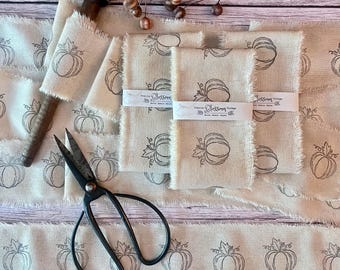 May include: A roll of beige fabric ribbon with a repeating dark brown pumpkin print and frayed edges, accompanied by a pair of black metal scissors and a wooden spool. A white paper band with the text Prairie Blossom Vintage wraps the fabric.