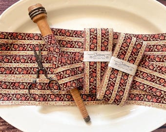 May include: A white oval platter displays fabric strips with a floral pattern in burgundy, cream, and peach. A wooden spool and vintage scissors are also on the platter. Two fabric bundles are labelled "prairie Blossom Vintage".