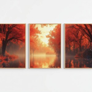 May include: A triptych of three framed wall art prints depicting a serene autumn forest landscape. The scene features vibrant red and orange foliage on trees reflected in calm, misty water, with a soft golden light glowing in the centre panel.