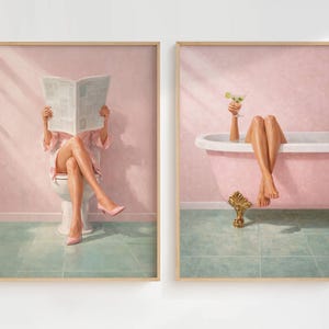 May include: A set of two framed wall art prints featuring a pink bathroom theme. The first print shows a person sitting on a white toilet reading a newspaper. The second print shows a person relaxing in a pink clawfoot bathtub holding a martini glass.
