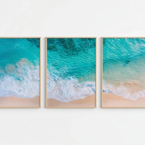 Puede incluir: Tres impresiones enmarcadas que muestran vistas aéreas de una playa. Cada impresión presenta una sección del océano turquesa que se encuentra con una orilla arenosa. La superficie del agua muestra olas y diferentes tonos de azul. Los marcos son de color madera clara.