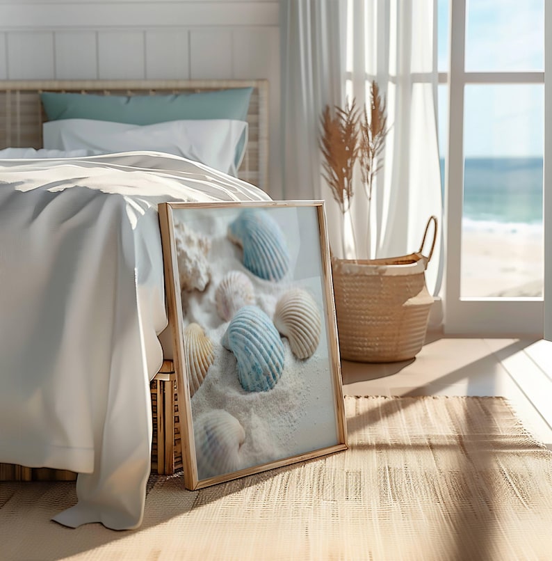May include: A rectangular framed wall art print featuring a collection of textured seashells in shades of white, cream, and soft blue resting on a bed of fine white sand, displayed in a light-toned wooden frame with a clean, simple border.