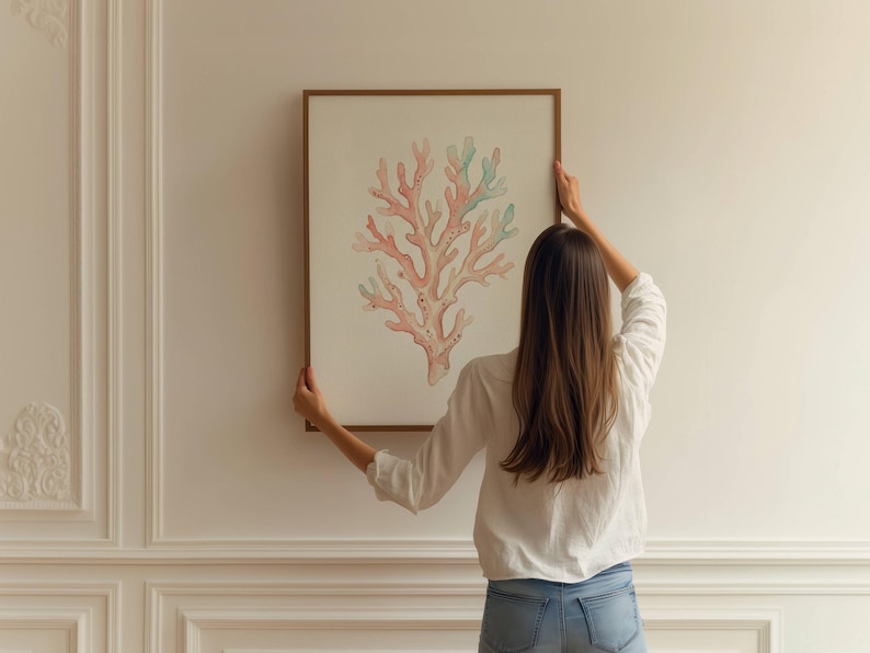 May include: A rectangular wall art piece featuring a detailed illustration of a branching coral structure in shades of soft pink and light green, encased in a thin wooden frame, displayed against a plain, off-white paneled wall surface.