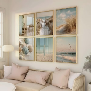 May include: A gallery wall set of six square framed prints featuring coastal scenes, including a beach house, sand dunes with tall grass, seashells on sand, a surfboard standing on a beach, and seagulls flying over ocean waves at sunset.