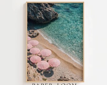 May include: A vertical wall art print featuring an aerial view of a sandy beach with rocky cliffs and turquoise water. Several pink and white striped beach umbrellas are arranged on the sand, each accompanied by a small chair, creating a coastal scene.
