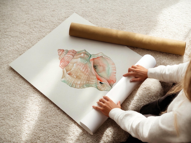 May include: A square white art print featuring a watercolor illustration of a conch shell in shades of soft pink, peach, and muted green. The shell is depicted with intricate spiral details and a textured surface, presented on a flat paper sheet.
