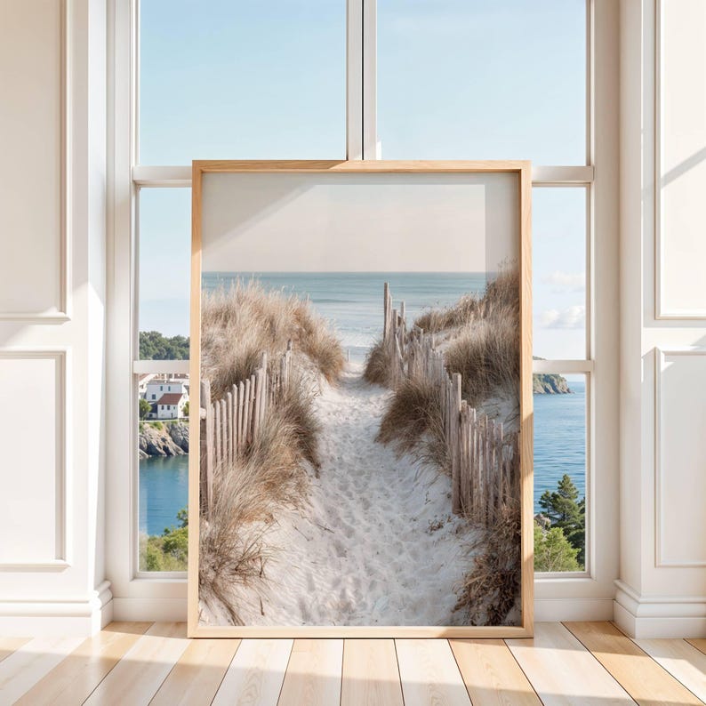 May include: A vertical framed wall art print featuring a sandy path leading toward the ocean. The path is bordered by tall, dry beach grass and weathered wooden picket fencing. In the distance, a calm sea meets a pale, soft-toned sky.