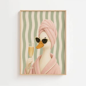 Könnte beinhalten: Ein gerahmter Wandkunstdruck, der eine weiße Ente mit einem rosa Handtuch auf dem Kopf und einem passenden rosa Bademantel zeigt. Die Ente trägt eine schwarze Cat-Eye-Sonnenbrille und hält ein hohes Glas mit goldenem Champagner vor einem wellenförmigen grün-weißen Hintergrund.