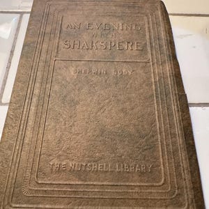 May include: A vintage book titled "An Evening with Shakspere" by Sherwin Cody, part of "The Nutshell Library." The cover is a textured, muted brown with embossed lettering and decorative borders, suggesting an antique aesthetic.