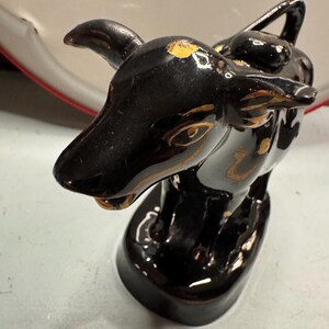 May include: Black ceramic figurine of a bull with gold accents. The bull is standing on a black base.