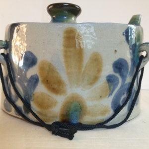 May include: A ceramic pot with a lid and a black cord handle. The pot is decorated with a blue and brown floral design.