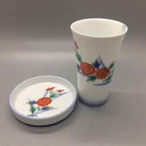 以下が含まれることがあります： 赤い、青い、緑の花で飾られた、白い陶器のカップとソーサーのセットです。