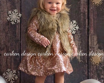 May include: A young girl wearing a rose gold sequin dress with a brown faux fur vest and a sparkly hair bow. She is standing in front of a wood background with snowflakes.