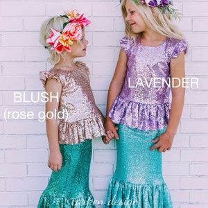 Puede incluir: Dos ni&ntilde;as con colas de sirena y tops de lentejuelas. La ni&ntilde;a de la izquierda lleva un top de color oro rosa y una corona de flores. La ni&ntilde;a de la derecha lleva un top de color lavanda y una corona de flores. El texto "BLUSH (rose gold)" est&aacute; a la izquierda y "LAVENDER" a la derecha.