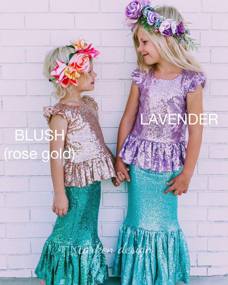 Puede incluir: Dos ni&ntilde;as con colas de sirena y tops de lentejuelas. La ni&ntilde;a de la izquierda lleva un top de color oro rosa y una corona de flores. La ni&ntilde;a de la derecha lleva un top de color lavanda y una corona de flores. El texto "BLUSH (rose gold)" est&aacute; a la izquierda y "LAVENDER" a la derecha.