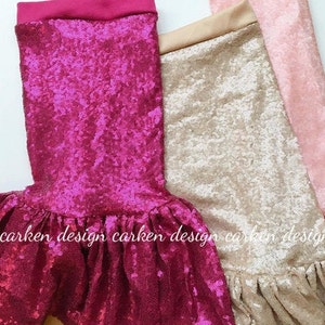 Op de afbeelding: Drie pailletten-zeemeerminstaarten in roze, goud en een diepe magenta kleur. De staarten zijn gemaakt van een glinsterende stof en hebben een gerimpelde onderkant.