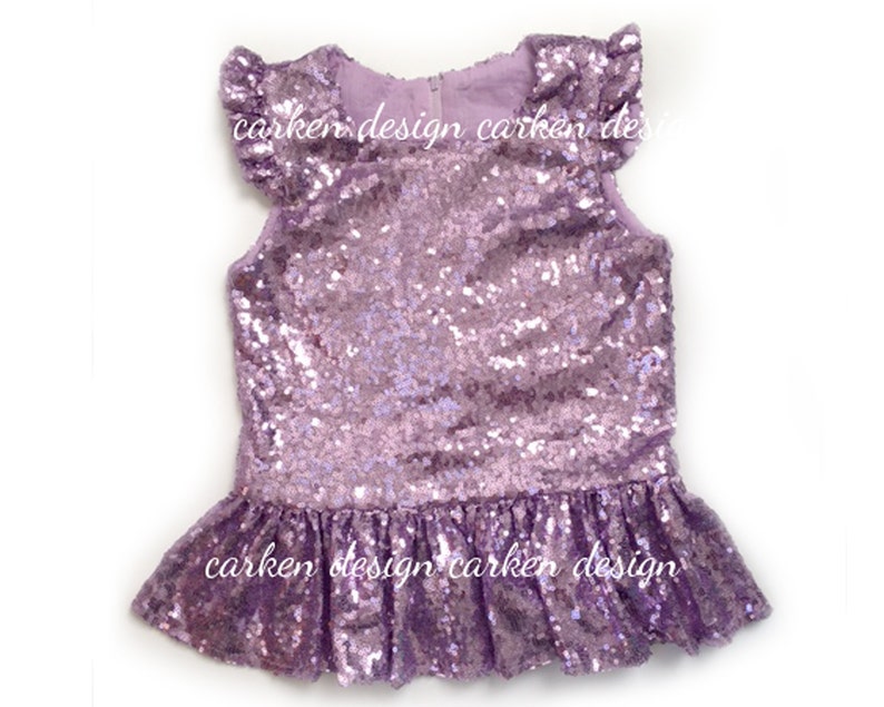 Puede incluir: Un top de lentejuelas color lavanda con un dobladillo con volantes y mangas cortas. El top tiene una marca de agua "carken design".