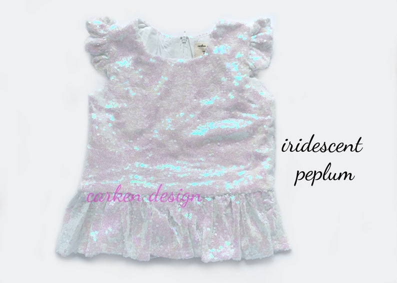 Puede incluir: Una blusa blanca de lentejuelas iridiscentes con un dobladillo de p&eacute;plum con volantes y mangas cortas. La blusa tiene un escote redondo y est&aacute; hecha de una tela suave y c&oacute;moda.