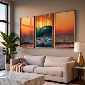 Puede incluir: Tres obras de arte enmarcadas que representan olas del océano al atardecer. Los marcos dorados resaltan colores vibrantes de naranja, azul y amarillo. El arte cuelga sobre un sofá beige con una manta rosa. Diseño moderno.