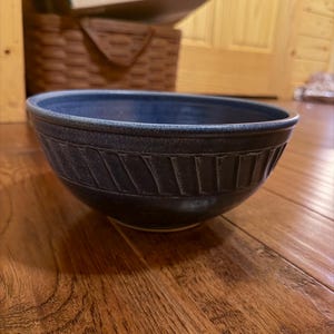 May include: A deep blue ceramic bowl with a smooth interior and a textured exterior featuring a band of vertical, slightly angled indentations around the upper circumference. The bowl has a rounded rim and a solid, dark blue glazed finish.
