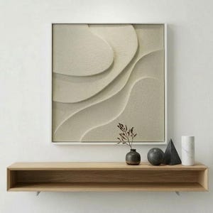 Può includere: Un'opera d'arte murale moderna con un design strutturato e stratificato in tonalità neutre è appesa sopra una mensola in legno. La mensola espone un piccolo vaso con una pianta, una sfera scura, una scultura triangolare nera e un oggetto cilindrico bianco.