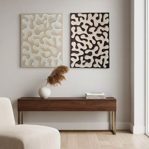 Könnte beinhalten: Zwei abstrakte Wandkunstwerke in neutralen Farbtönen. Eines ist beige mit weißen Formen, das andere dunkelbraun mit cremefarbenen Formen. Darunter eine Konsole aus dunklem Holz mit goldenen Beinen, eine weiße Vase und ein cremefarbener Stuhl.