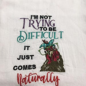Puede incluir: Paño de cocina blanco bordado con la frase "I'm not trying to be difficult, it just comes naturally." El paño presenta un bordado de un pollo con gafas y pañuelo. El texto es de varios colores.