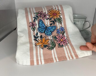 Ramo de flores con mariposas revoloteando sobre una toalla de rayas rosa (48 x 73 cm)