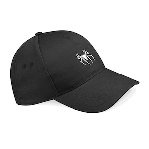 Könnte beinhalten: Eine schwarze Baseballkappe mit einem weißen, gestickten Spinnenemblem in der Mitte des Vorderteils. Die Kappe hat eine strukturierte Krone, einen gebogenen Schirm und zwei kleine Belüftungsösen an der Seite des Stoffes.