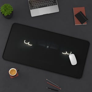 May include: Black rectangular mousepad with a car headlight design. A white computer mouse is on the right side of the mousepad. A laptop, a small potted plant, a cup of coffee, and stationery are also on the dark gray surface.