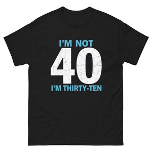 以下が含まれることがあります： 「I'M NOT 40 I'M THIRTY-TEN」の文字が白と水色でプリントされた黒いTシャツ。数字の40はひび割れたような加工が施されています。ユーモラスなグラフィックTシャツ。