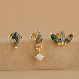 May include: Three pairs of gold earrings. One pair is a stud with a diamond-shaped green stone. Another pair has a dangling diamond-shaped green stone with a small, round, clear stone. The third pair has three green leaf-shaped stones.
