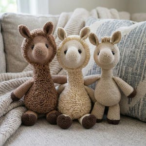 May include: Three handmade crochet llama dolls in shades of brown and beige sit on a gray couch. Each llama has a unique color and texture, with dark brown hooves and small black eyes. The dolls are soft and cuddly.
