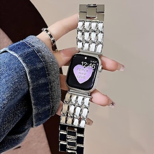 May include: Silver-toned Apple Watch with a white and black chain-link band. The watch face displays the time 12:46 and the words "PEACE AND LOVE" on a purple heart-shaped background. A matching bracelet is also visible.