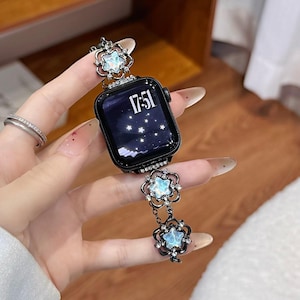 May include: Black smartwatch with a decorative strap. The strap features star-shaped charms with iridescent centers and rhinestone accents. The watch face displays the time 17:51 and a starry night design. The strap is attached to the watch with small chains.