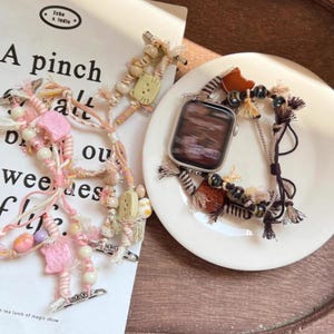 May include: An Apple Watch with a decorative band featuring a mix of beads, tassels, and woven elements in brown, beige, and orange. A second beaded accessory with pink and white beads is also present.