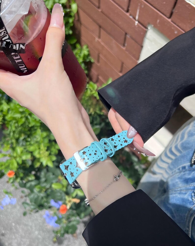 May include: A light blue watch band with a star pattern. The band is made of a soft material and has a silver buckle. The watch band is worn on a wrist with a silver bracelet.