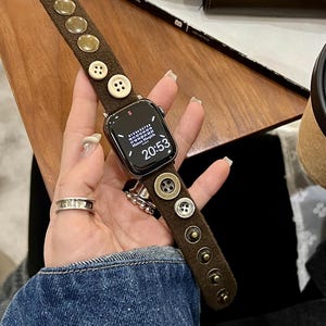 May include: A brown watch band with gold and silver buttons and studs. The watch face displays the time as 20:53. The band is made of a soft, textured material.