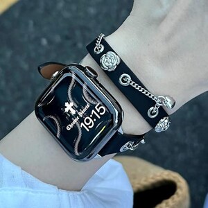 May include: Black smartwatch with a decorative black leather band and silver-tone accents. The watch face displays the time as 19:15 and the words "Chrome Hearts". A matching black leather bracelet with silver chain and floral details is also shown.