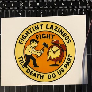 Könnte beinhalten: Ein runder Aufkleber mit dem Text "FIGHTINT LAZINESS FIGHT TILL DEATH DO US PART". Er zeigt einen Comic-Mann mit Hammer und schmelzendem Wecker in Gelb, Orange und Schwarz.