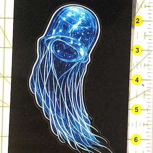 May include: A sticker featuring a blue jellyfish design with white outlines on a black background. The jellyfish has a detailed, glowing appearance. A small, colorful graphic is in the lower left corner.