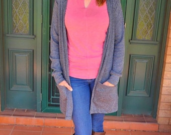 May include: A woman wearing a grey cardigan over a pink t-shirt, blue jeans, and brown knee-high boots.