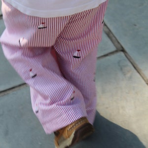 May include: Red and white striped pants with a small sailboat design. The pants are worn by a person walking on a stone path.
