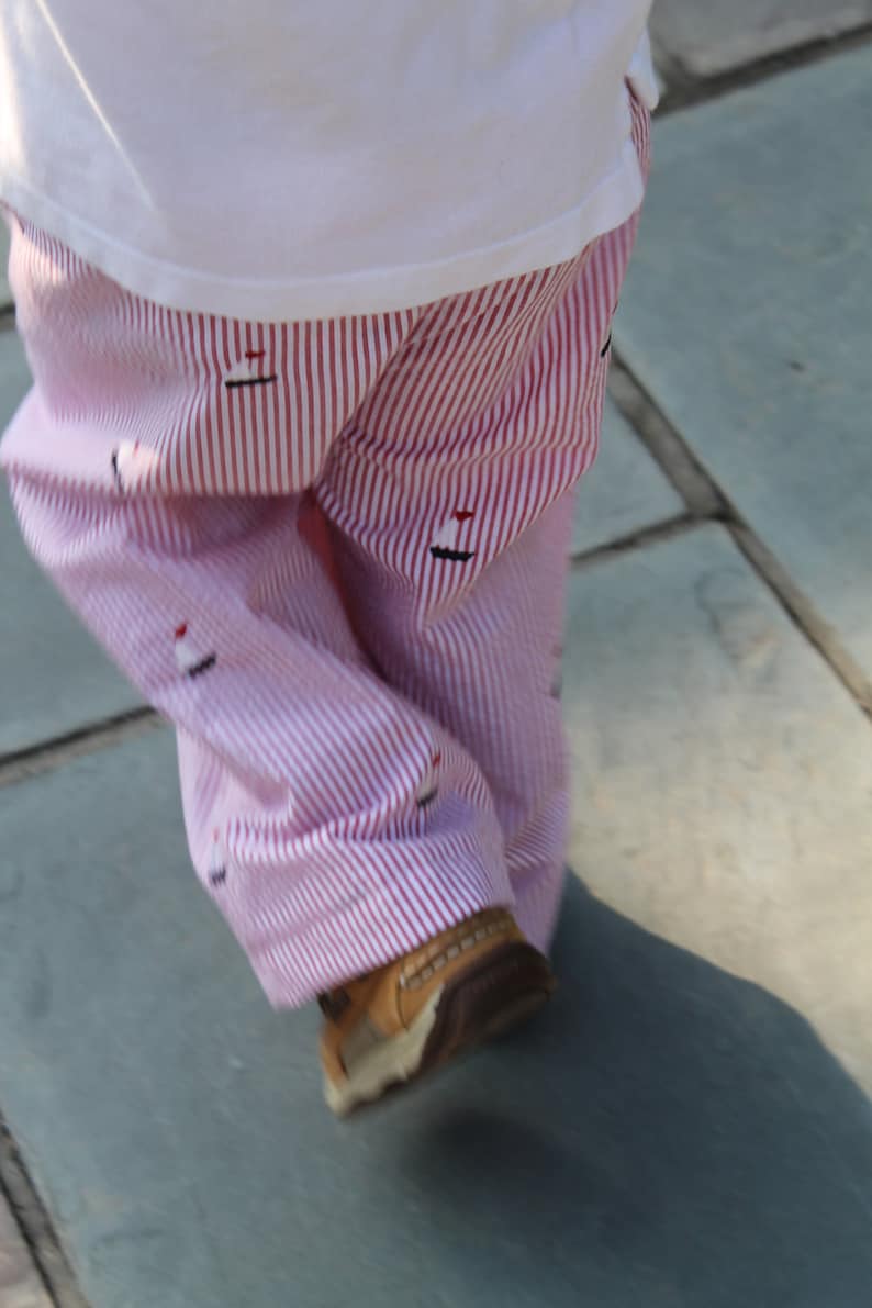 May include: Red and white striped pants with a small sailboat design. The pants are worn by a person walking on a stone path.