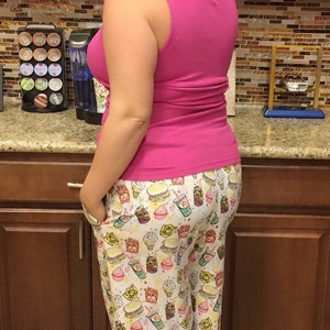 May include: A woman wearing a pink tank top and white pajama pants with a fast food print. The pants feature images of hamburgers, french fries, ice cream cones, and soda cups.