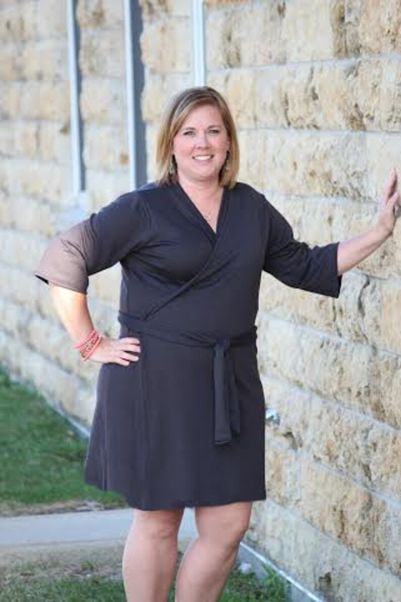 May include: A woman wearing a dark grey wrap dress with a long sleeve and a tie at the waist.