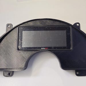 May include: A black dashboard gauge panel with a rectangular screen in the center. The panel has a curved shape with mounting tabs on each side. The screen has the Holley logo.