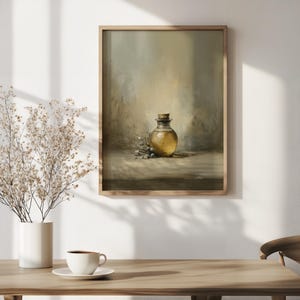 May include: A framed art print depicts a still life with a glass bottle filled with golden liquid, likely olive oil, and a cork stopper. The bottle is accompanied by olive branches. The artwork is in a muted color palette of beige, brown, and gold.
