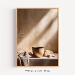 May include: A framed print featuring a still life with a beige ceramic bowl, sliced bread, and a linen cloth. The background is a textured beige wall with shadows. The text "WHERE FAITH IS" is at the bottom.